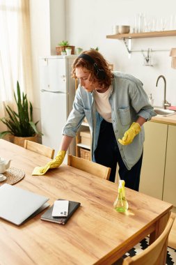 Yakışıklı genç adam sıcak evinde eldiven ve kulaklık takarak mutfak masasını temizliyor..