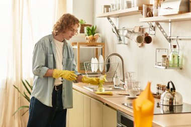 Kıvırcık saçlı genç adam mutfak yüzeylerini temizler. Yeni, hoş bir ortam yaratır..