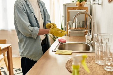 Genç bir adam modern bir mutfakta bulaşıkları yıkamaya hazırlanıyor..