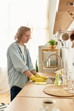 Parlak öğleden sonra ışığı sıcacık mutfağı dolduruyor. Yakışıklı bir genç adam odak ve özenle temizliyor..