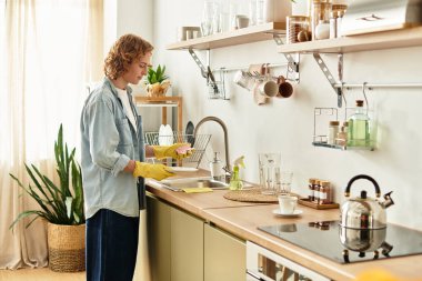 Çekici özellikleri olan genç bir adam parlak, davetkar bir mutfak tezgahında bulaşıkları yıkıyor..