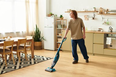 Genç bir adam şık bir mutfakta yerleri temizlemek için süpürge kullanarak temizlik yapar..