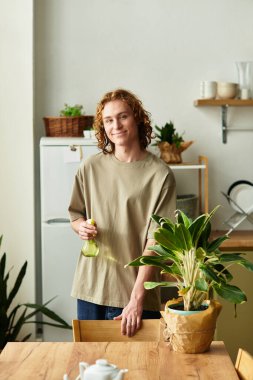 Yakışıklı genç adam evde duruyor, elinde bir sprey şişeyle yeşillikle ilgileniyor..