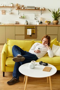 Yakışıklı genç bir adam, parlak sarı bir kanepede rahat bir şekilde uzanır ve akıllı telefonuyla meşgul olur..