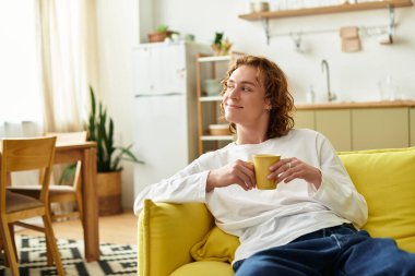 Yakışıklı bir genç adam parlak bir kanepede oturuyor, sıcak bir içkinin tadını çıkarıyor ve evde eğleniyor..