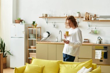 Yakışıklı genç bir adam parlak bir mutfakta duruyor, kahvesini yudumluyor ve telefonuna odaklanıyor..