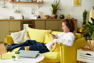 Yakışıklı bir genç adam parlak sarı bir kanepede rahatça oturur, müzik ve rahatlığın tadını çıkarır..