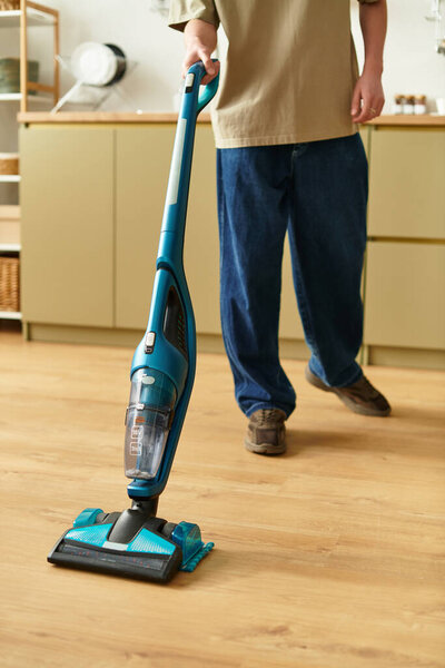 Молодой человек с радостью очищает свое пространство современным вакуумом на теплых деревянных полах..