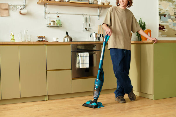 A young man casually vacuums the floor in his stylish kitchen.