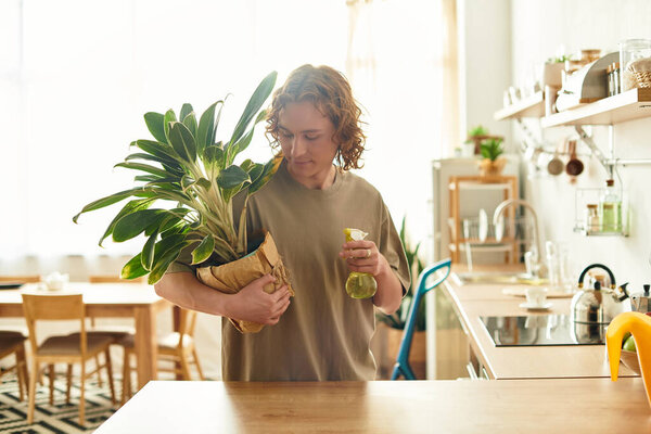 A handsome young man tends to a green houseplant in a stylish kitchen during a sunny afternoon.