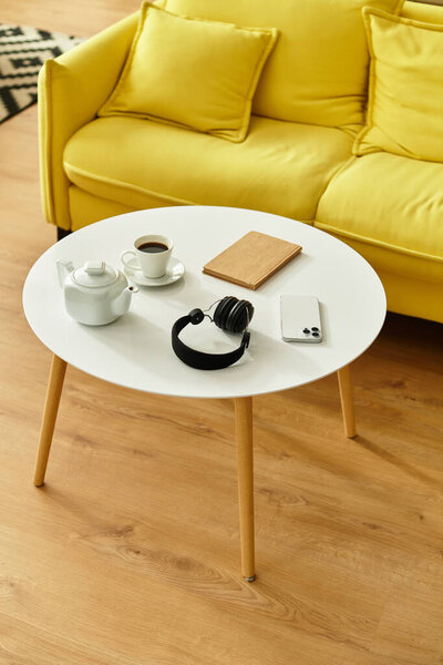 White modern aesthetic coffee table with smartphone, headphones, cup and kettle in cozy house.