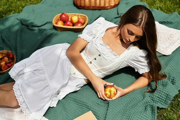 Genç bir kadın piknik battaniyesinde dinleniyor, taze elmaların ve doğanın tadını çıkarıyor..