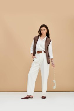 Güzel genç bir kadın, şık kıyafetlerini bir stüdyoda güven içinde poz verirken sergiliyor..