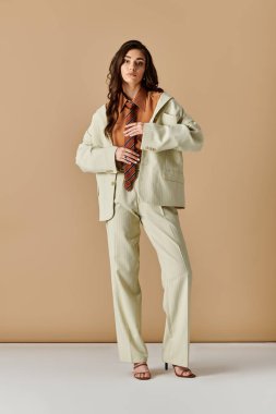 Sofistike takım elbiseli, kravatlı genç bir kadın şık bir stüdyoda kendine güvenen bir poz verdi..