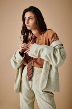 Uzun kahverengi saçlı güzel bir kadın. Stüdyoda şık bir takım elbise ve kravat giyiyor..