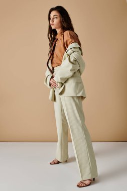 Uzun kahverengi saçlı güzel bir genç kadın şık bir takım elbise içinde rahatça poz verir..