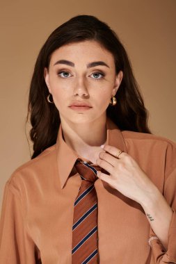 Uzun kahverengi saçlı güzel bir kadın şık bir elbise ve kravat takıyor..