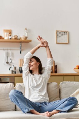 Genç bir kadın rahat dairesinde kanepede dinlenirken esniyor ve gülümsüyor..