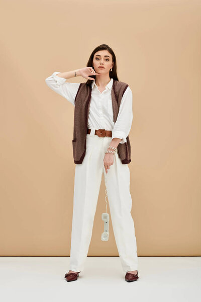 Красивая молодая женщина с длинными каштановыми волосами излучает уверенность в стильном наряде, элегантно позируя.