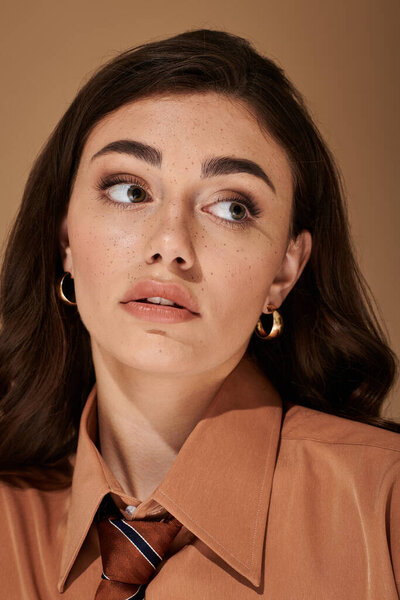 A fashionable young woman with long brown hair showcases her elegance dressed in a chic attire.