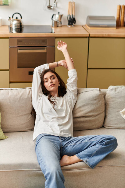 Красивая молодая женщина с каштановыми волосами комфортно отдыхает в своей квартире, растягиваясь.