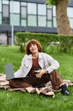 Kıvırcık saçlı genç kadın canlı bir parkta kahvenin tadını çıkarırken dışarıda laptopuyla çalışıyor..