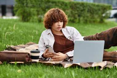 Kıvırcık saçlı kadın yaz boyunca laptopuyla çalışırken battaniyeye uzanıyor..