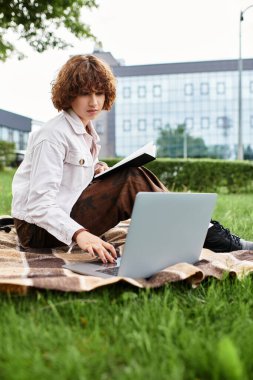 Kıvırcık saçlı serbest çalışan, yemyeşil bir parktaki bir laptopta rastgele çalışır..