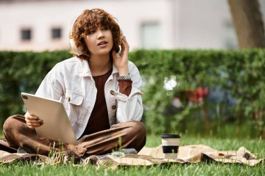 Kıvırcık saçlı genç bir kadın battaniyede dinleniyor, kahvesinin ve tabletinin tadını çıkarıyor..