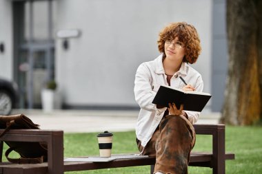 Kıvırcık saçlı kadın ofis binasının dışındaki deftere yazıyor..