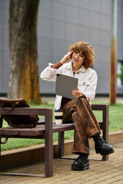 Freelancer güneşli bir yaz gününün keyfini çıkarıyor. Canlı yeşil bir parkta tablet üzerinde çalışıyor..