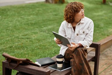 Kıvırcık saçlı bir kadın bu yaz güneşli bir parkta uzaktan çalışıyor..
