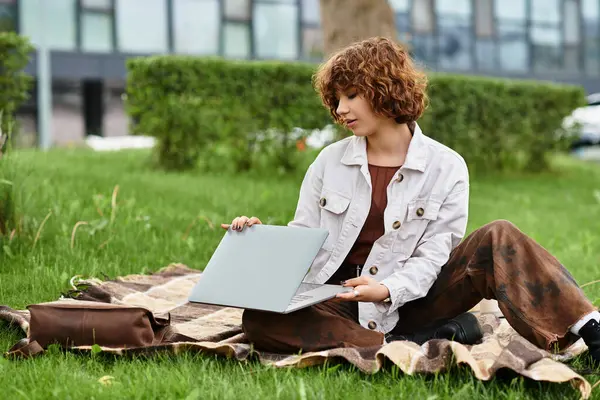 Kıvırcık saçlı genç bir kadın güneşli bir parkta dizüstü bilgisayarıyla çalışırken serbest yaşamı kucaklıyor..