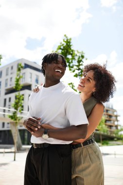 Neşeli genç bir çift yaz güneşinin altındaki şehir manzarasında birlikte neşeli bir anı paylaşıyor..