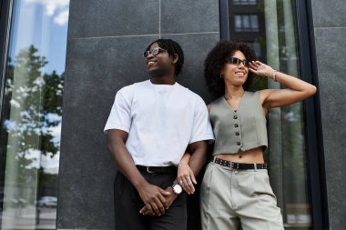 Moda kıyafetleri içinde genç bir çift gülümsüyor ve sıcak bir günde şehirde neşeli bir anı paylaşıyor..