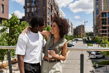 Genç bir Afrikalı Amerikalı çift, canlı bir şehirde kahve içerken gülümsüyor..