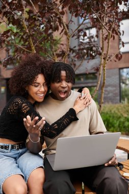 Genç bir Afro-Amerikan çifti, şehir ortamında laptoplarında neşeli bir şekilde iş birliği yapıyor..