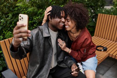 İki genç yetişkin mutlu bir anı paylaşıyor, kentte bir arada otururken selfie çekiyorlar..