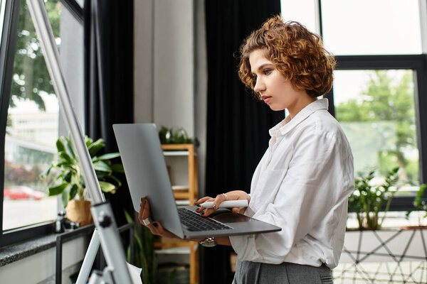 В современном офисе молодая деловая женщина с кудрявыми волосами пристально работает над своим ноутбуком..