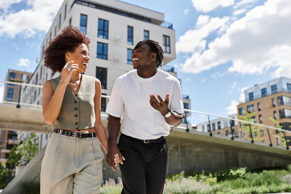 A young African American couple strolls hand in hand, laughing and enjoying their date together.