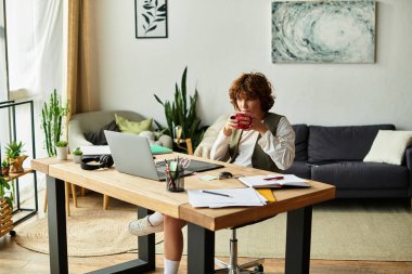 Kıvırcık saçlı genç bir kadın, parlak bir alanda dizüstü bilgisayarındaki görevlere odaklanırken kahvesini yudumluyor..