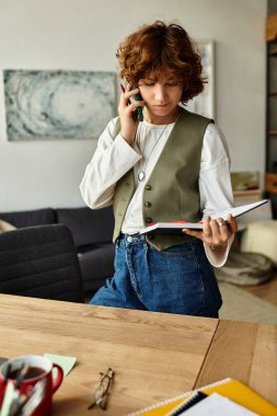 Kıvırcık saçlı genç bir kadın telefonda çoklu görev yapıyor ve şık dairesinde notları gözden geçiriyor..