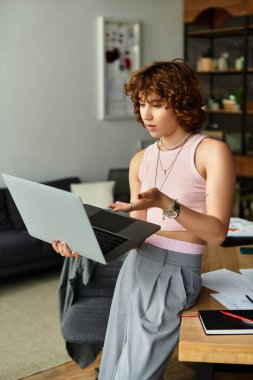 Kıvırcık saçlı kadın, şık bir dairede çalışırken dizüstü bilgisayarıyla meşgul oluyor..