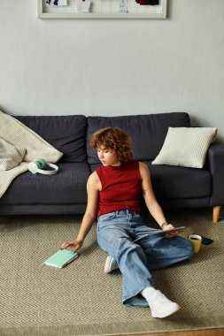 Genç bir kadın kendini evinde dinlenirken defterine dalmış yerde rahatça oturuyor.