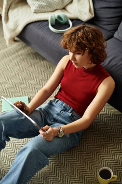 Kıvırcık saçlı kadın evinde yaratıcı aktiviteler yaparken yerde dinleniyor..