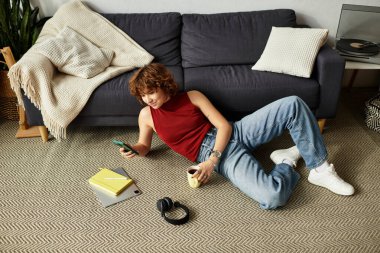 Kıvırcık saçlı kadın şık dairesinde telefonuyla bağlantı kurarak zaman geçirmekten hoşlanıyor..