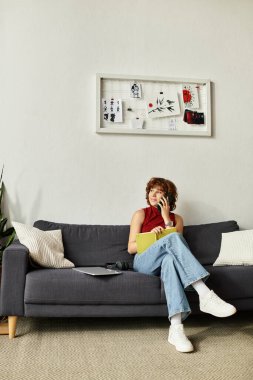 Kıvırcık saçlı kadın kanepesinde dinleniyor, notlar yazarken bir sohbete dahil oluyor..