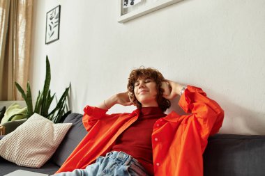 Kıvırcık saçlı genç bir kadın şık dairesinde rahatlıyor, huzur saçıyor..