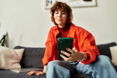 Canlı kıyafetli genç bir kadın akıllı telefonunu kullanırken modern dairesinde dinleniyor..