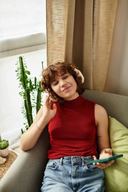 Huzurlu bir yaz günü geçiren genç bir kadın, telefonunu kullanırken rahat dairesinde dinleniyor..